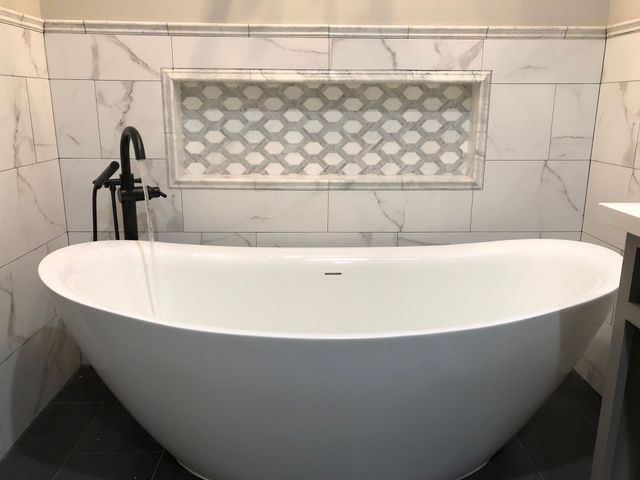 Freestanding bath with black fixtures in a finished tiled room